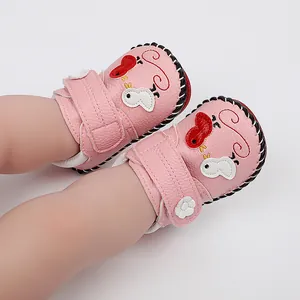 Primer plano de zapatos rosas para bebé con pájaros de dibujos y costuras a mano.