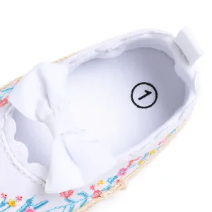 Detailopname van witte babyschoentjes voor meisjes met bloemenborduurwerk en strik