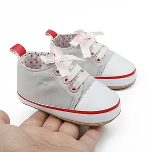 Close-up of grey baby walking shoes with pink ribbon laces held in hand for scale