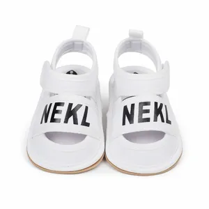 Close-up of white baby summer walking sandals featuring black NEKL printed text