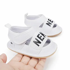 Close-up view of white baby walker sandals featuring NEXT lettering and velcro strap