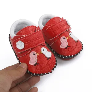 Detalle de los zapatos de bebé rojos cosidos a mano con diseño de pájaro de dibujos