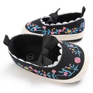 Gedetailleerd overzicht van geborduurd bloemenpatroon en strik op zwarte babyschoenen