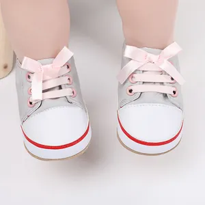 Close-up of gray baby pre-walker shoes with pink ribbon bows and soft white soles.