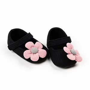 Close-up of black knitted baby girl princess shoes with pink flower decoration