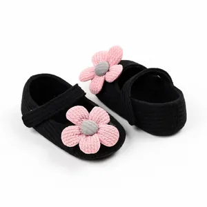 Detailed close-up of black knitted baby walking shoes with pink yarn flower decoration