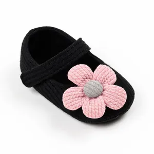 Detail view of black knitted baby princess shoe with a large pink floral decoration