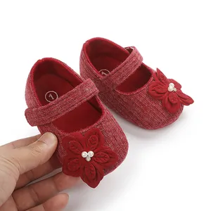 Dettaglio di scarpine rosse da principessa per neonata con fiori e perle in mano.