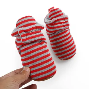 Gros plan de bottes d'hiver rayées rouges pour bébé tenues à la main pour taille.