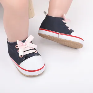 Detail view of navy baby girl walking shoes with pink ribbon laces on infant feet
