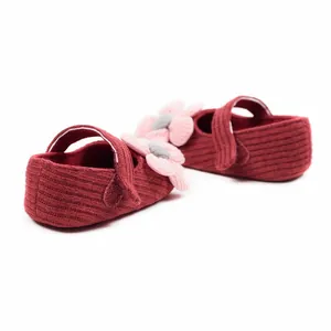 Close-up of elegant red knit baby princess shoes with soft pink decorative flowers.