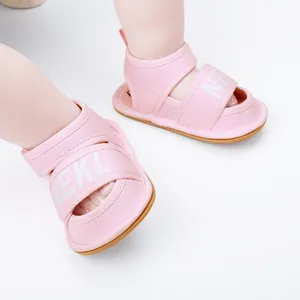 Close-up detail of pink soft-soled infant walker sandals with white lettered straps.