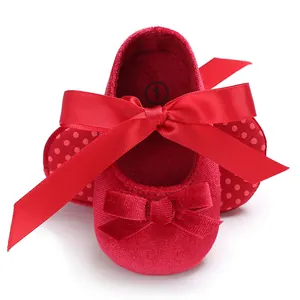 Gros plan de chaussures bébé en velours rouge avec un élégant nœud en ruban de soie.