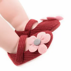 Detailed close-up of red ribbed fabric baby shoes with a soft pink flower detail