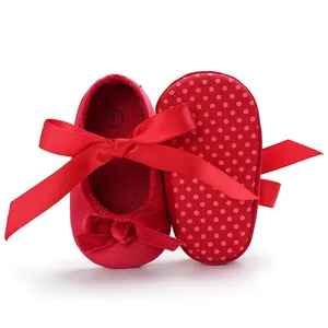 Gros plan de chaussures de bébé rouges à semelle souple, points antidérapants et nœud.