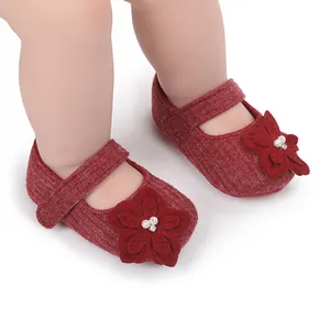 Primo piano di scarpine in maglia rosso scuro per neonata con dettaglio fiore di perle.