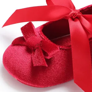 Vue macro montrant la texture en velours rouge et le nœud élégant sur les chaussures bébé.