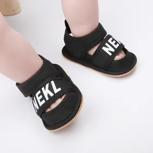Detailed view of black infant summer sandals with NEKL letter print worn on baby feet