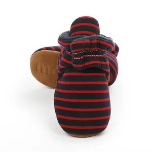 Détail de chaussons bébé doux et chauds à rayures bleu marine et rouge, semelle brune.