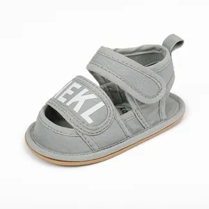 Detailed close-up view of gray fabric baby walking sandals with white lettered velcro strap