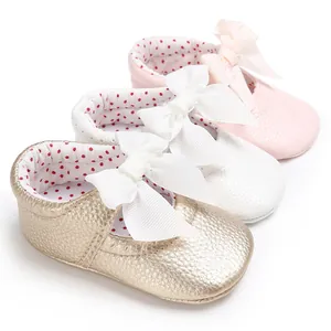 Vista detallada de zapatos de bebé princesa con lazos en cuero de color oro, blanco y rosa.