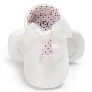 Vista detallada de los zapatos de princesa blancos para bebé con un gran lazo de cinta