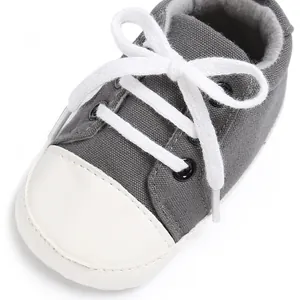 Detailansicht grauer Leinwand Babyschuh mit weißen Schnürsenkeln und Gummikappe.