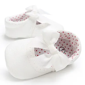 Primer plano de elegantes zapatos de princesa para bebé blancos con lazo y puntos.