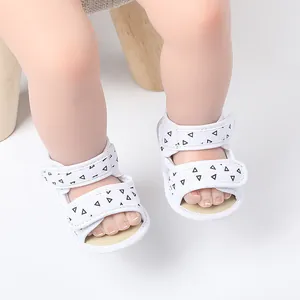 Detail view of white baby sandals featuring black triangle patterns and secure velcro straps