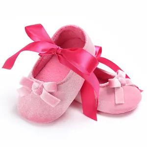 Gros plan de chaussures de bébé en velours rose avec nœud en ruban et semelle souple.