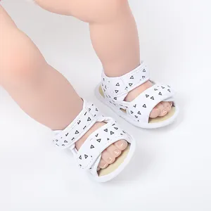 Close-up of white baby sandals with triangle pattern and velcro straps on infant feet
