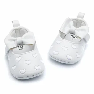 Detail of white baby princess shoes with embroidered heart patterns and a bow