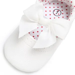 Primer plano de zapatos blancos de princesa para bebé con lazo y forro de lunares