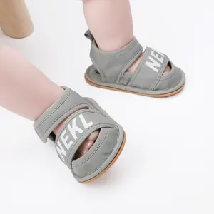 Close-up view of grey fabric baby summer sandals featuring a white NEKL printed strap.