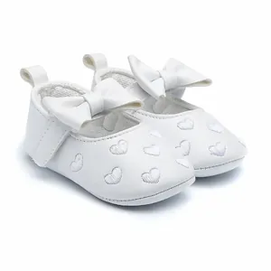 Close-up view of white baby girl princess shoes with embroidered heart patterns and large bow