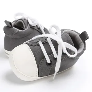 Nahaufnahme grauer Segeltuch-Babyschuhe mit weißen Schnürsenkeln und weicher weißer Sohle