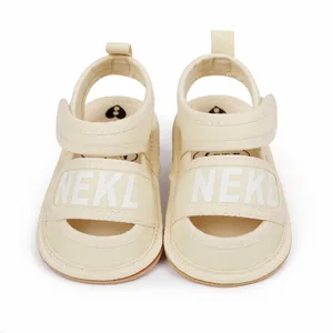 Close-up front view of beige canvas baby summer sandals featuring NEKL printed straps.