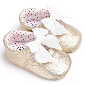 Detalle de zapatos dorados de princesa para bebé con elegantes lazos blancos grandes
