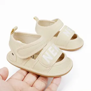 Close-up view of beige baby summer first walker sandals with adjustable strap held in hand