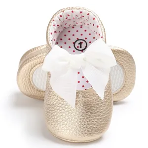 Detalle de zapatos de princesa dorados para bebé con un lazo blanco decorativo grande