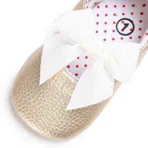 Detalle de zapato de princesa dorado para bebé decorado con un gran lazo blanco
