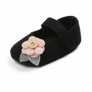 Nahaufnahme eines schwarzen Strick-Babyschuhs für Mädchen mit einer rosa Stoffblume