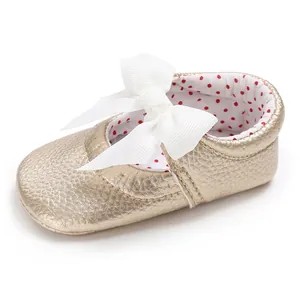 Vista detallada de zapato de princesa dorado para bebé con un gran lazo blanco