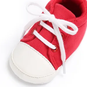 Nahaufnahme eines roten Segeltuch-Babyschuhs mit weißen Schnürsenkeln und Lederkappe