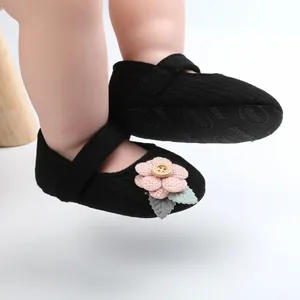 Detailansicht der schwarzen Baby-Mädchenschuhe mit einer rosa Blume und Holzknopf