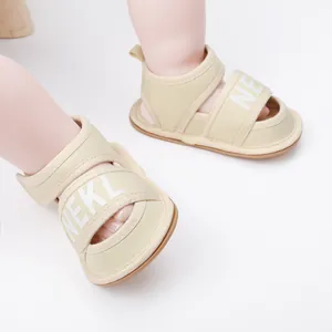 Close-up of beige infant walking sandals with NEKL letter print on velcro straps