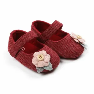 Nahaufnahme dunkelroter Strickschuhe für Babymädchen mit rosa Blume und Holzknopfdizierung.
