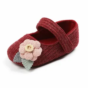 Nahaufnahme eines roten gestrickten Babyschuhs für Mädchen mit Blumenverzierung