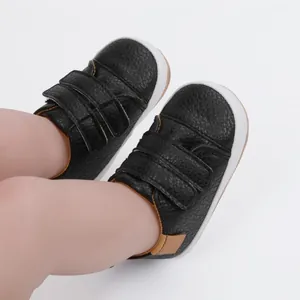 Close-up of black faux leather baby shoes with velcro straps and soft white soles.