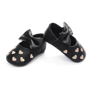 Nahaufnahme schwarzer Kunstleder-Prinzessinnenschuhe für Babys mit Herzstickerei und Schleife